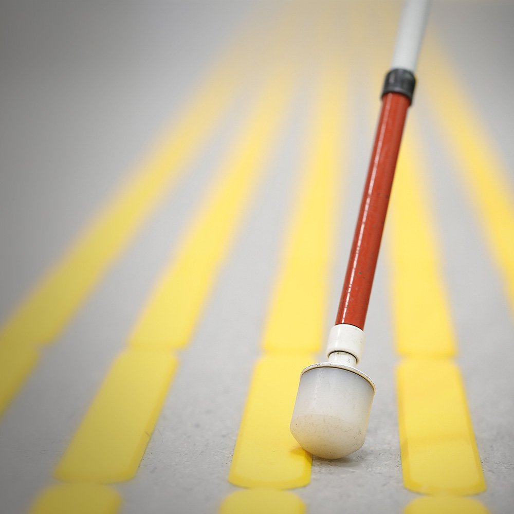 Nahaufnahme eines Langstocks auf einem Blindenleitsystem