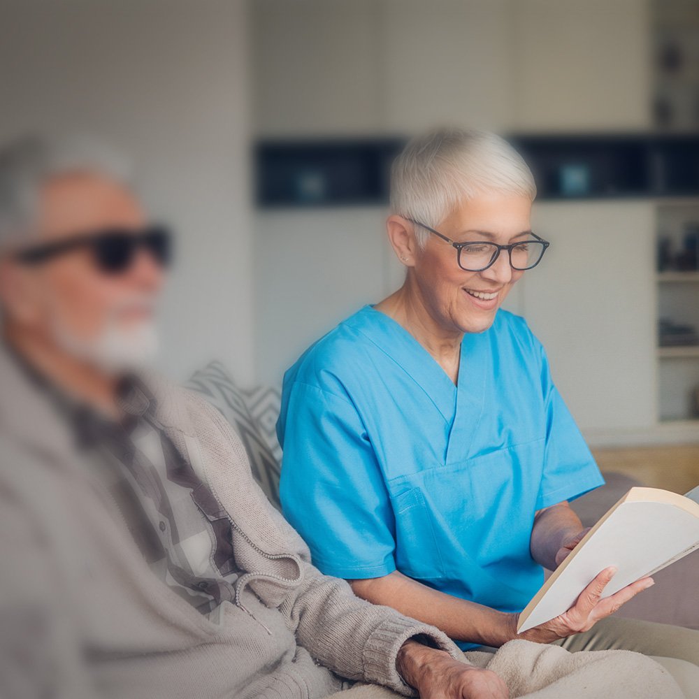 Eine Pflegekraft liest einer sehbehinderten Person aus einem Buch vor