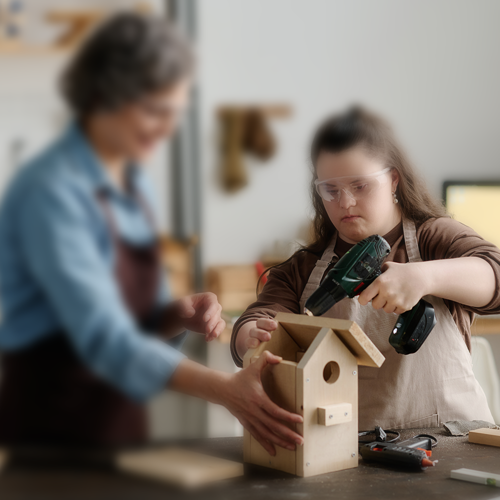 Eine junge geistig beeinträchtigte Frau arbeitet mit einer Betreuerin in einer Werkstatt