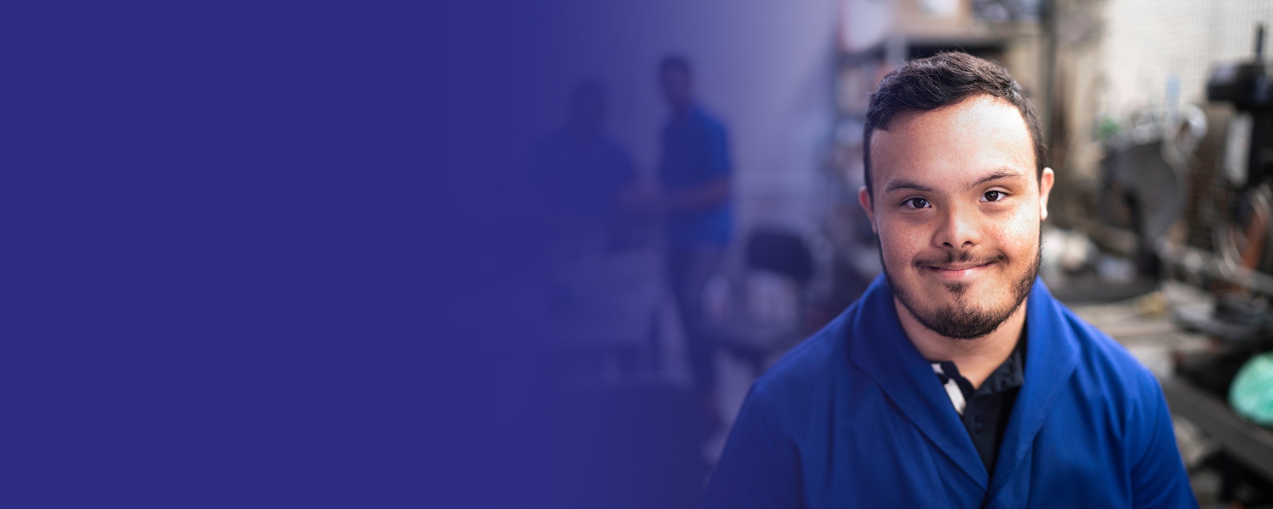 Junger Mann mit Behinderung in einer Werkstatt lächelt in die Kamera