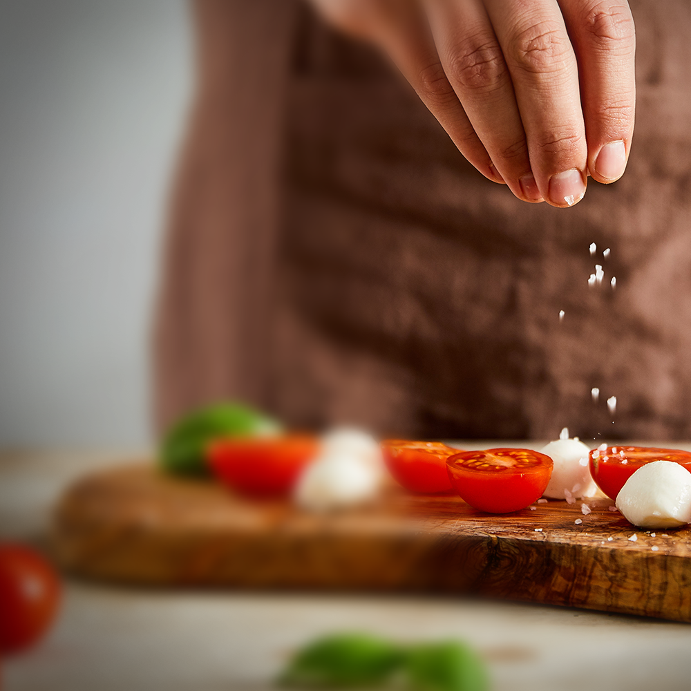 Eine Hand streut Salz auf ein Brett mit Tomaten und Mozzarella