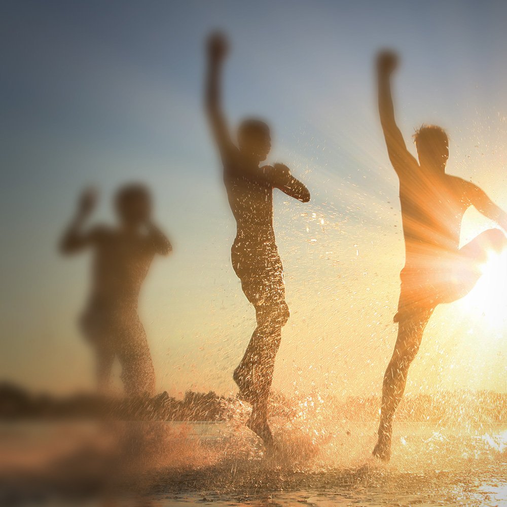 Im Wasser hüpfende Menschen mit strahlender Sonne im Hintergrund