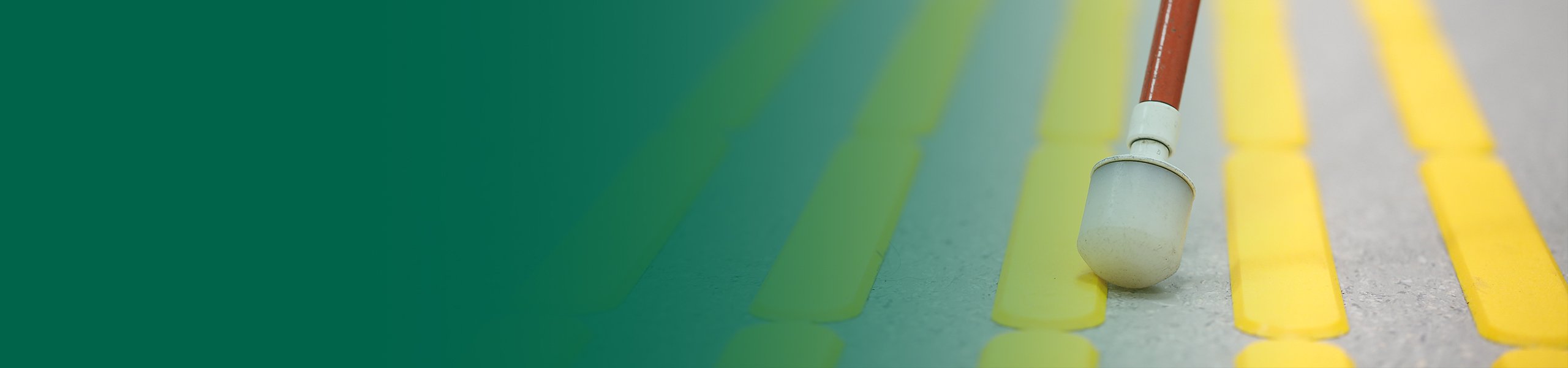 Nahaufnahme eines Langstocks auf einem Blindenleitsystem mit Verlaufsüberlagerung