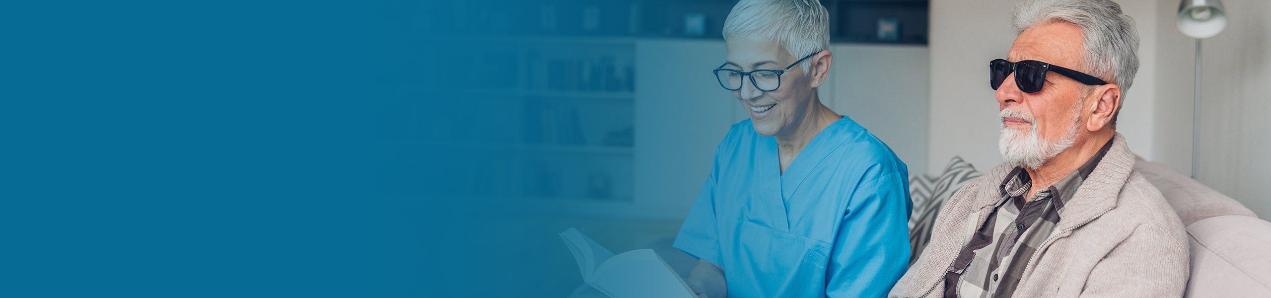 Eine Pflegekraft liest einer sehbehinderten Person aus einem Buch vor