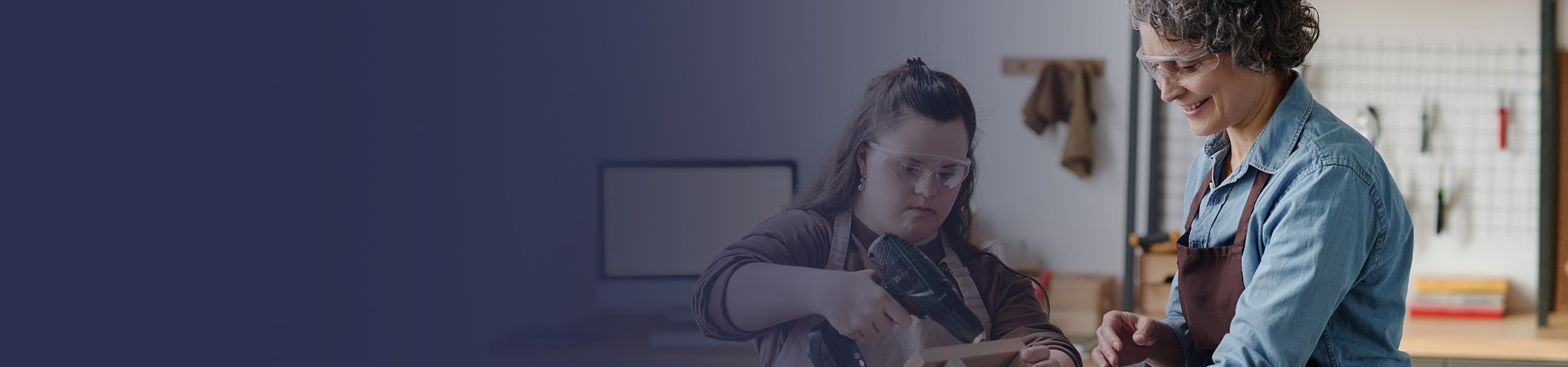 Eine junge geistig beeinträchtigte Frau arbeitet mit einer Betreuerin in einer Werkstatt