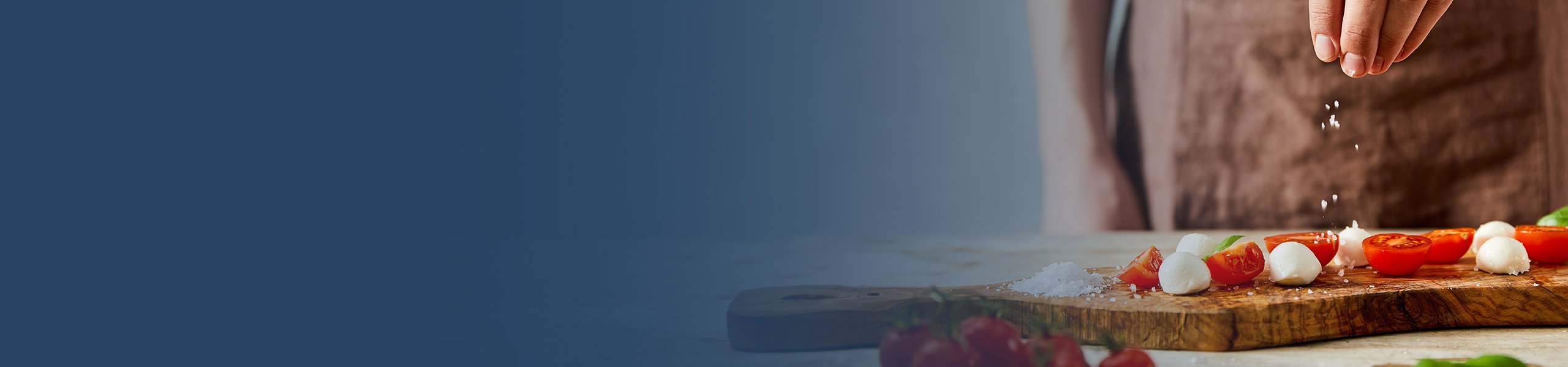 Eine Hand streut Salz auf ein Brett mit Tomaten und Mozzarella