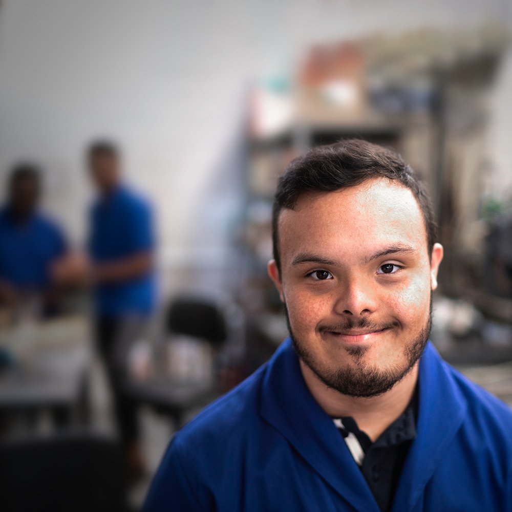 Junger Mann mit Behinderung in einer Werkstatt lächelt in die Kamera