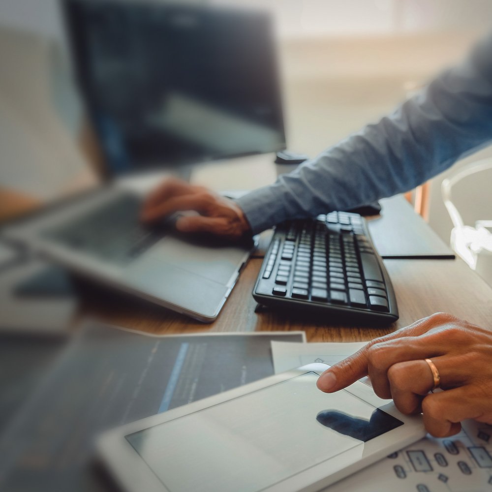 Eine Person bedient einen Laptop und ein Smartphone mit je einer Hand